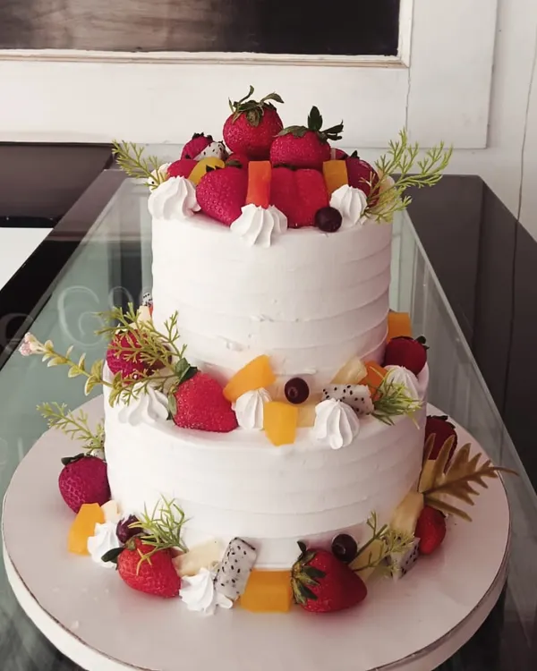 A refreshing two-tiered cake generously decorated with a variety of fresh fruits. This design features whole strawberries, dragon fruit, and orange slices, perfect for a summer celebration.