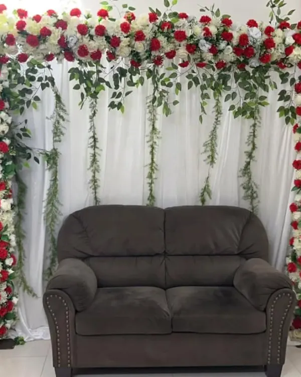 A simple yet beautiful photo corner created in a living room. I built a floral arch using red and white roses with trailing greenery around the client's own sofa, instantly creating a dedicated spot for pictures.