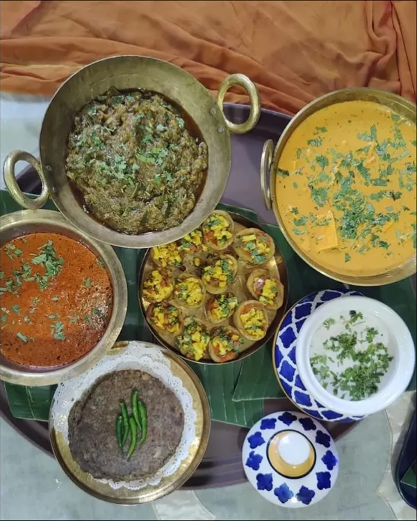 A traditional Indian feast featuring a variety of classic dishes. This spread includes Shahi Paneer, a mixed vegetable dish, raita, and roti, all served in authentic brassware.