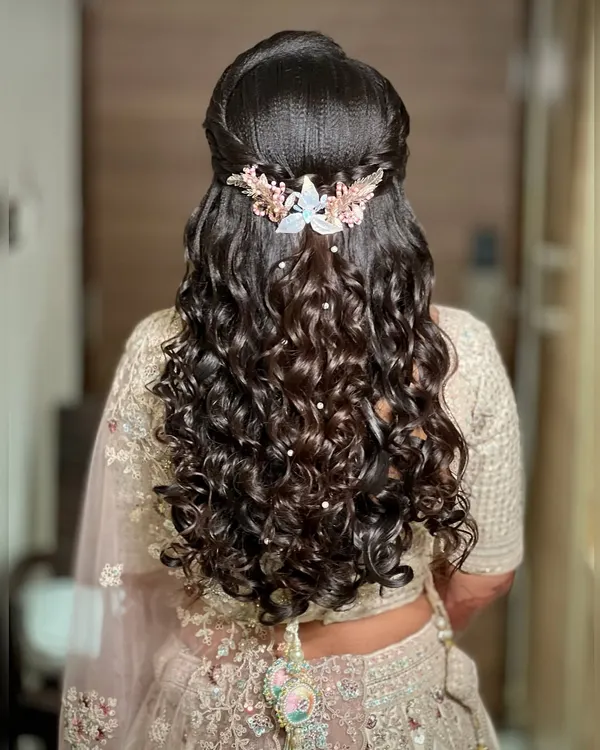 A stunning example of a half-up, half-down hairstyle with voluminous curls, perfect for a reception. The look is completed with a beautiful pearl and crystal hair accessory.