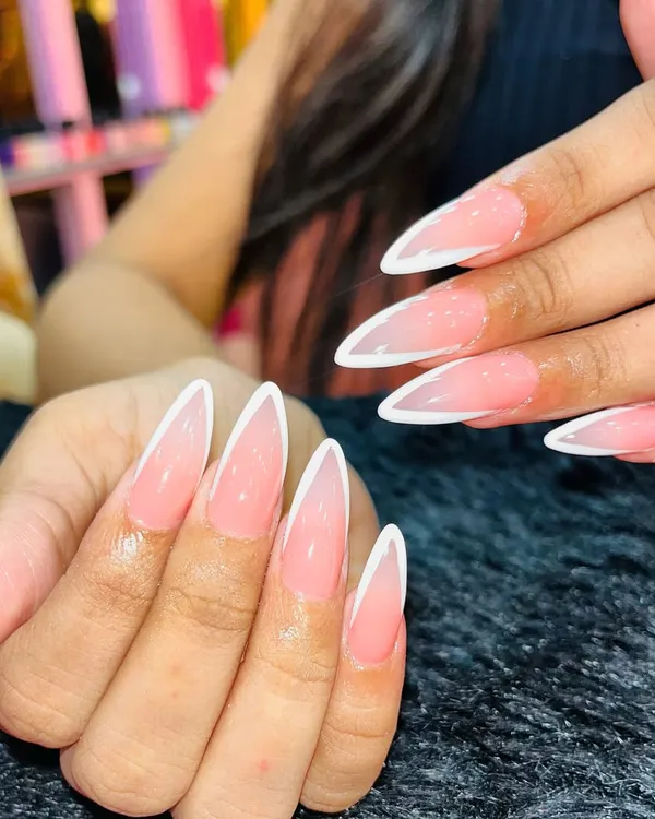 A dramatic and sharp take on the French manicure. This look features a soft pink ombre base on long stiletto nails with a crisp, deep "V" white tip, creating a very elegant and elongated effect.