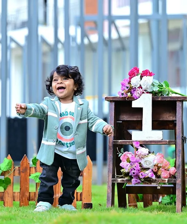 A burst of pure happiness! This outdoor shot captures the joy of turning one, with a simple fence and floral prop that complements the natural background.