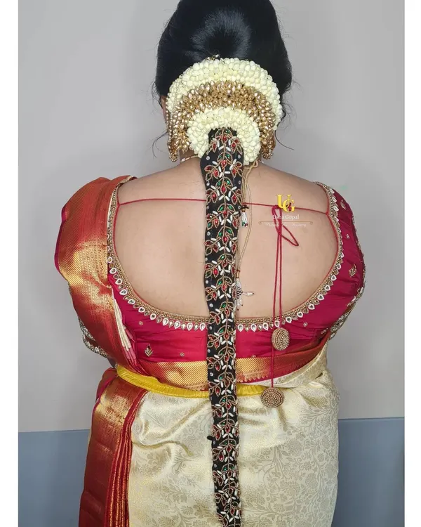 A traditional South Indian bridal hairstyle for Akshatha's muhurtham, featuring a long braid adorned with intricate hair jewellery and a jasmine flower arrangement.
