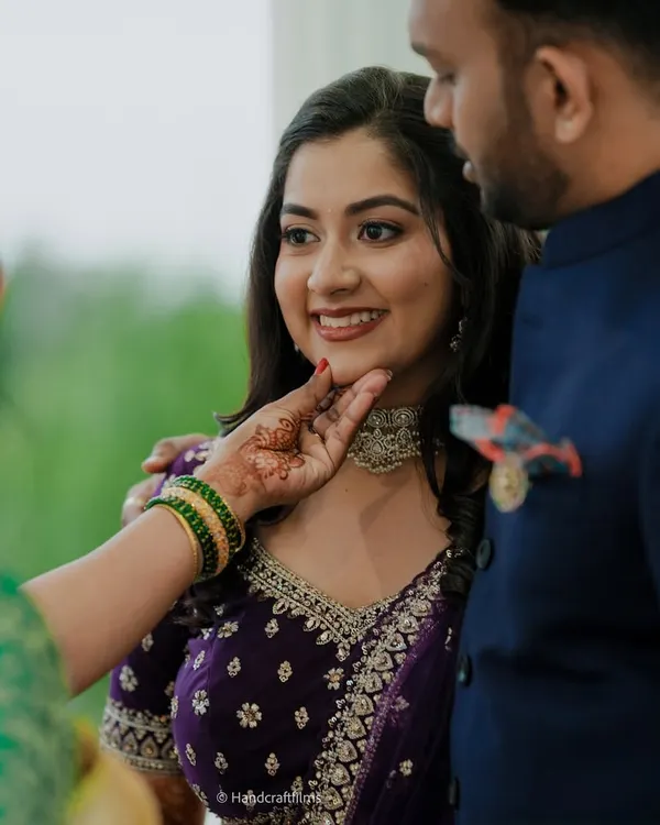 A beautiful candid moment from an engagement ceremony. The bride's makeup is soft and romantic, with a focus on glowing skin and a natural lip, perfectly complementing her purple lehenga.