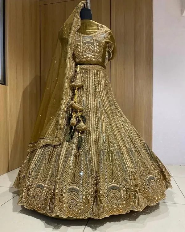 A stunning golden lehenga displayed on a mannequin. This piece is covered in intricate embroidery and sequins, perfect for a bride who wants a glamorous, shimmering look.