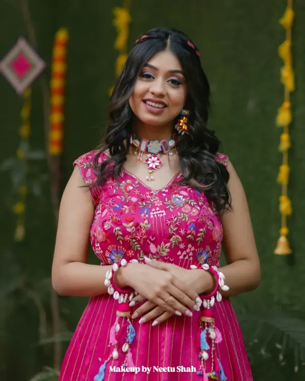 A radiant Haldi bride. This soft glam look features a pop of pink on the eyes, glowing skin, and a modern braided hairstyle, perfectly matching her vibrant outfit and shell jewelry.