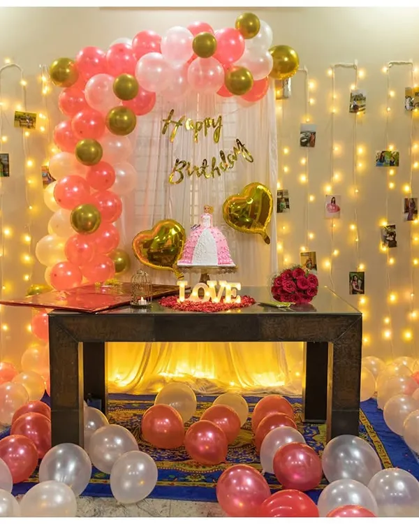 A full view of our popular indoor birthday setup. We combine a pink and gold balloon arch with a curtain of fairy lights and scattered floor balloons to create a fun and photo-ready party zone.