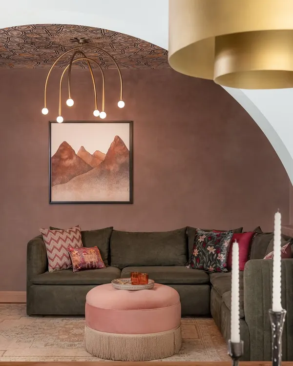 A close-up of the living room in the Quiet Ornate home. We love layering textures and patterns, like the deep rosé tinted walls, the intricate wallpaper on the ceiling, and the mix of cushions on the olive sofa.
