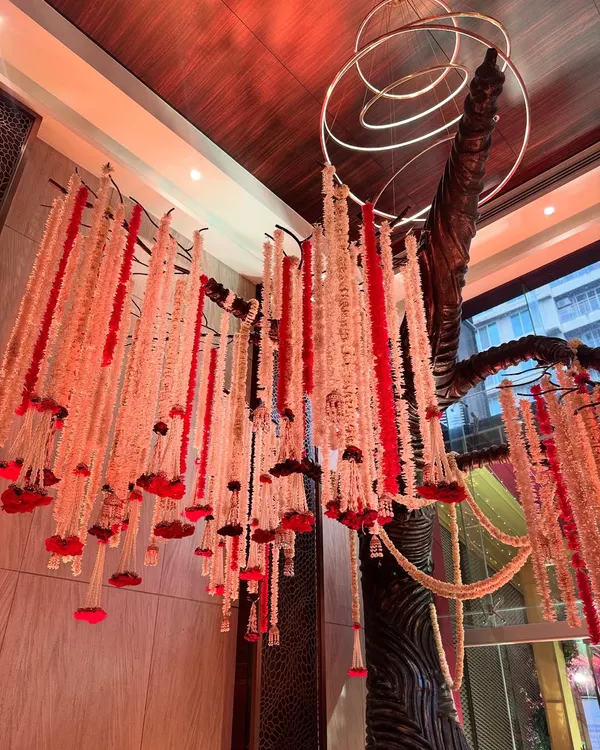 A dramatic ceiling installation featuring a cascade of red and white floral strings hanging from a sculptural tree-like structure, creating a true work of art.
