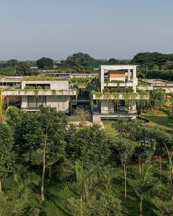 An aerial view of a weekend home where the architecture is completely immersed in a dense, green landscape. The design features green roofs and cascading plants that soften the concrete structure, making it one with its surroundings.