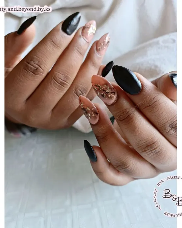 A dramatic and elegant design featuring black gel polish on acrylic extensions. The accent fingers have a stunning black and nude marble effect, elevated with scattered gold flakes for a touch of luxury.