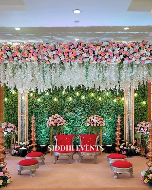 This lush Vidhi Mandap combines a verdant green wall with a canopy of cascading pink and white flowers. The traditional red seating provides a striking contrast, creating a sacred and beautiful space.