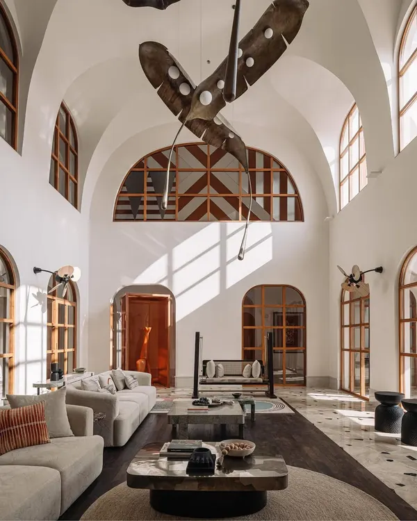 This double-height living room in our Rehethaan project captures our love for dramatic volumes, natural light, and art. The space is defined by its grotto-inspired architecture, grand arched windows, and a stunning, custom-designed leaf installation that feels like it's floating in mid-air.