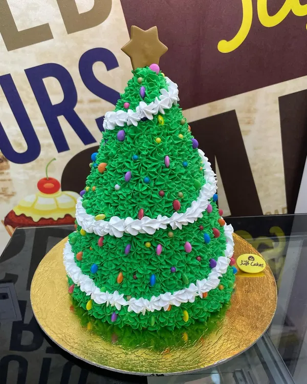 A custom 3kg Christmas tree cake, intricately decorated with green buttercream frosting, colorful sprinkles as lights, and a gingerbread star on top.