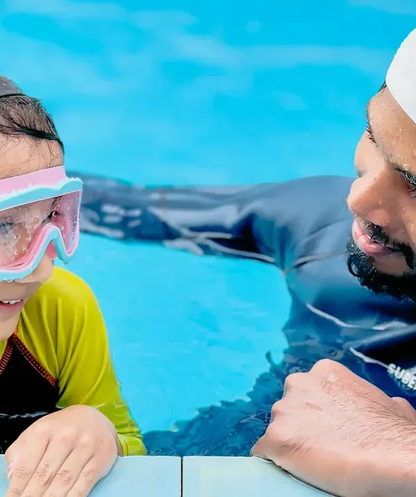 A coach provides one-on-one encouragement to a young swimmer at the edge of the pool. These moments of personal connection are key to building a child's confidence.