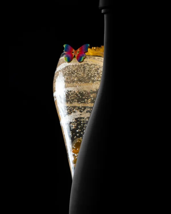 An interplay of sensational silhouettes. This shot captures the elegant form of our Peach and Lavender Bellini next to the bottle, highlighting its delicate bubbles and butterfly garnish.