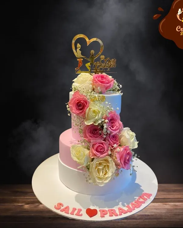 This stunning three-tier engagement cake combines classic white and soft pink, adorned with a spiral of fresh roses. It’s a timeless design that perfectly captures the romance of the occasion for the happy couple.