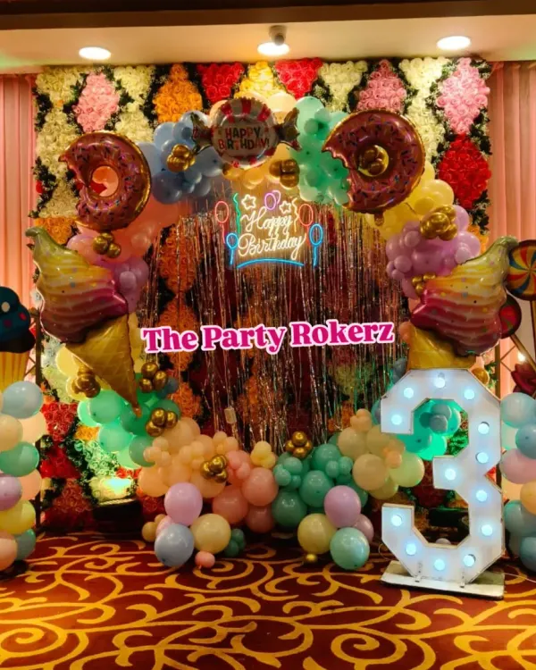 A delicious-looking Candyland theme for a 3rd birthday. I used a flower wall backdrop, a shimmer curtain, and a balloon arch decorated with giant donut, ice cream, and cupcake props.