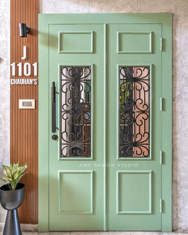 A statement entrance door painted in a refreshing sage green, featuring classic paneling and wrought iron grilles for a touch of vintage elegance.