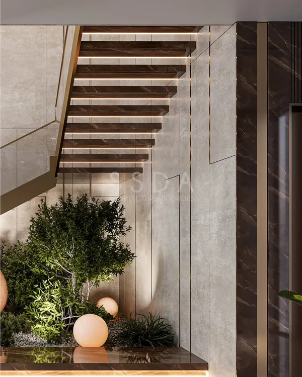 We believe greenery shouldn't be confined to the outdoors. In this villa, we designed a small garden bed directly beneath the floating staircase, turning a simple circulation space into a vibrant focal point with lush plants and soft, spherical lights.