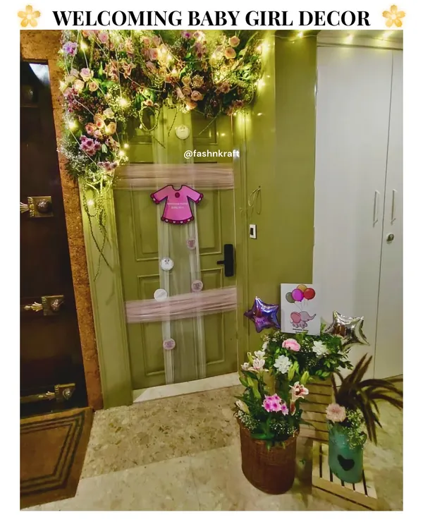 A charming welcome for a baby girl, with a floral arch and fairy lights adorning the front door. The decor includes sweet details like a onesie-shaped balloon and floral baskets, creating a warm and inviting homecoming.