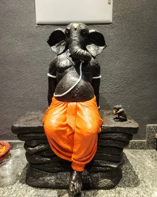 A modern interpretation of Lord Ganesha, sculpted in a relaxed posture. This custom FRP statue features a textured black finish with vibrant orange dhoti, created for a client in Gurgaon.