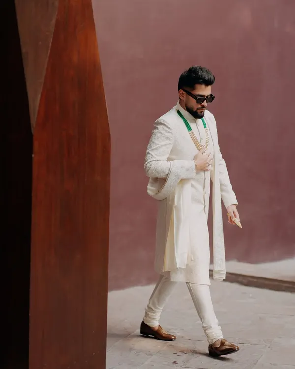 A stylish portrait of the groom, Shrey, looking dapper in his white sherwani and sunglasses. This shot captures his cool confidence and modern style on his wedding day.