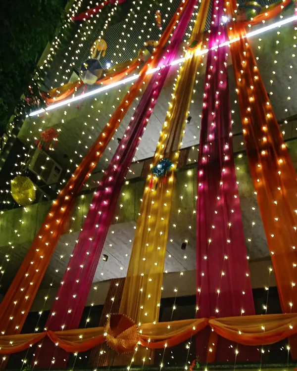 I make sure your house glows at night, creating that perfect 'shaadi ka ghar' feeling. This full building decoration uses colorful drapes and thousands of fairy lights to create a magical welcome for your guests.