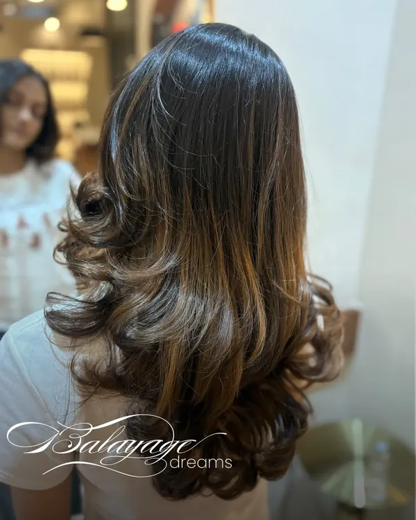 This is what balayage dreams are made of. We created these soft, dimensional layers of color to melt into her natural hair, finished with bouncy curls to show off the seamless blend.