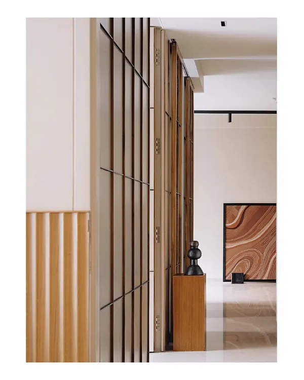 This entire wall is clad in a paneling inspired by Japanese shoji screens, using thin teak wood verticals and black metal batons. It discreetly hides several doors and storage spaces, creating an illusion of connectivity and adding length to the passage.