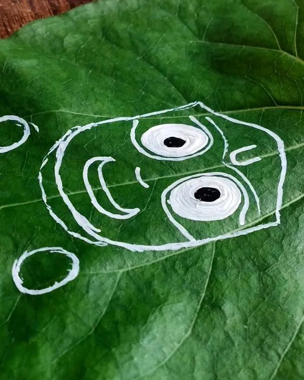 The first step in creating my Pipal leaf art is outlining the iconic form of Lord Jagannath. I use white paint to create a clear guide on the green leaf, ensuring the proportions are perfect before adding color.