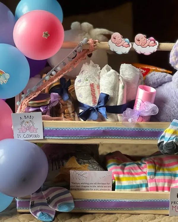This two-level newborn essentials hamper is both beautiful and functional. The top tier holds diapers and a plush toy, while the bottom has neatly folded baby clothes and socks, all decorated with a "Promoted to Mommy" sticker.