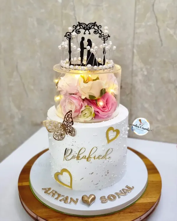 A beautiful two-tier cake for a Roka celebration. The clear spacer tier filled with flowers and fairy lights adds a touch of magic, making it a truly unique centerpiece for the happy couple.