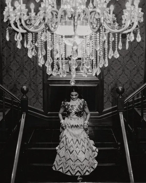 A timeless black and white portrait of the bride on her Sangeet night. The grand chandelier and elegant staircase create a classic, dramatic setting for this beautiful moment of anticipation.