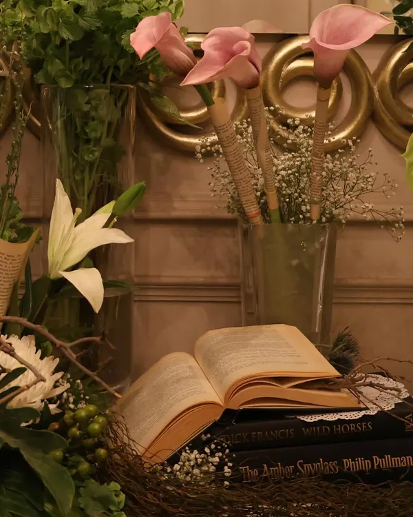 A close-up of our vintage-themed decor, featuring pink calla lilies and an open book set against a backdrop of lush greenery. This type of arrangement is perfect for creating an elegant, literary feel.