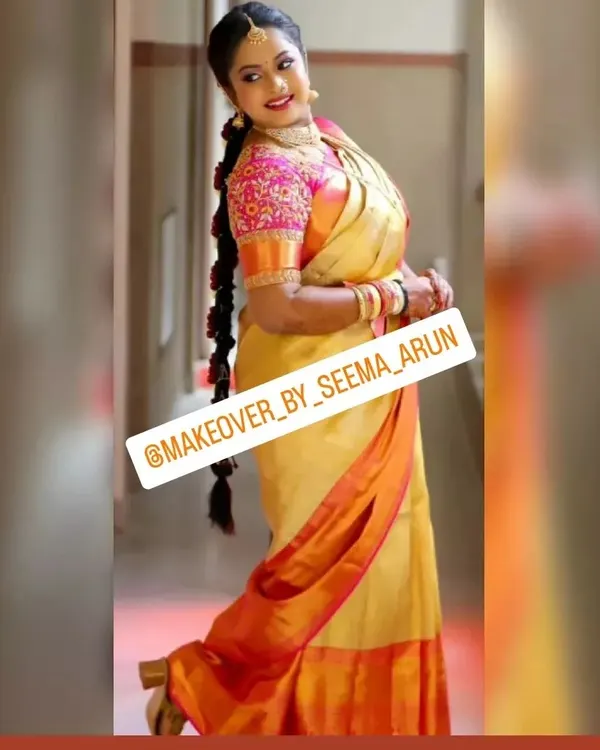 A full-length view of a happy bride ready for her muhurtham. This showcases the complete look, from the expertly draped Kanchipuram silk saree to the traditional long braid hairstyle, ensuring she looks and feels her best.