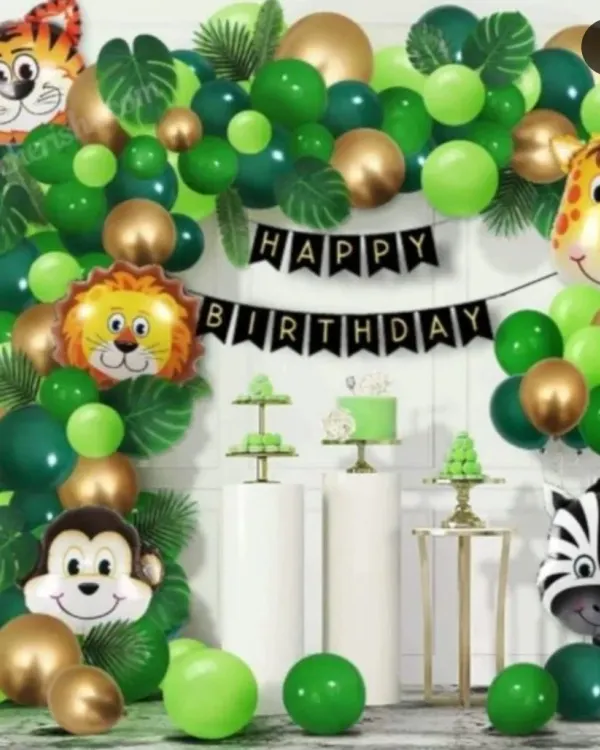 A classic jungle safari themed birthday party. This setup features a green and gold balloon arch, friendly animal face foil balloons including a tiger, lion, and monkey, and pedestals for the cake and treats.