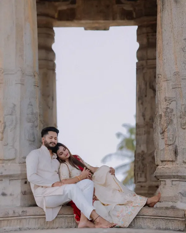 A quiet moment of rest between stone pillars at Melukote. The couple's traditional outfits complement the ancient architecture, creating a serene and timeless portrait.