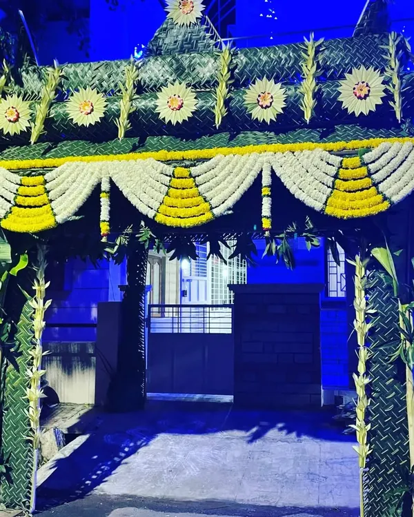 This traditional entrance toran is made from woven coconut leaves and banana stems. The arch is decorated with intricate patterns and garlands of white and yellow flowers, creating a grand welcome for a home ceremony.
