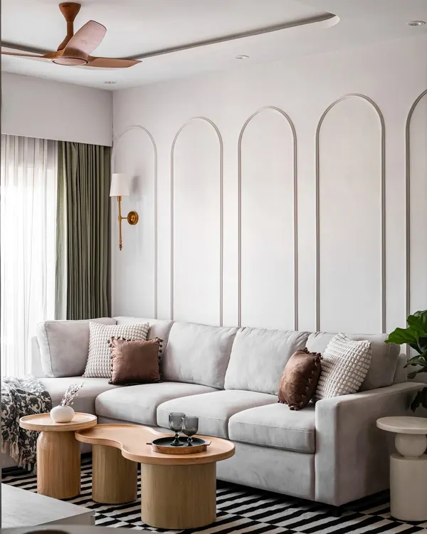 We designed this luxurious living room with a focus on creating a serene and sophisticated atmosphere. The large, comfortable L-shaped sofa is perfect for family time, and the wall is adorned with elegant arched mouldings. The organic-shaped wooden coffee tables and a striped rug add texture and warmth to the space.
