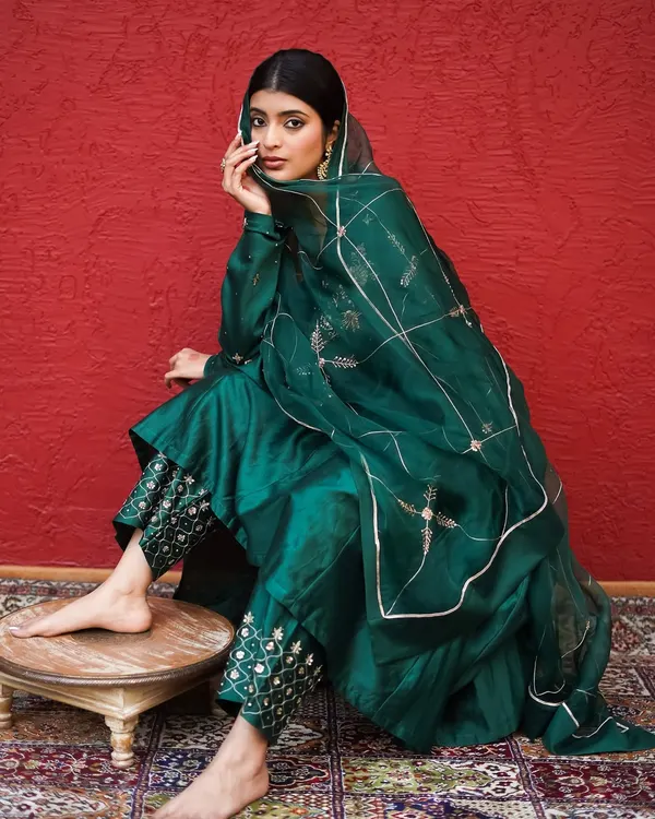 A seated pose that beautifully displays the fall of the emerald green fabric and the detailed embroidery on the pants. The composition draws attention to the craftsmanship of the ethnic attire.