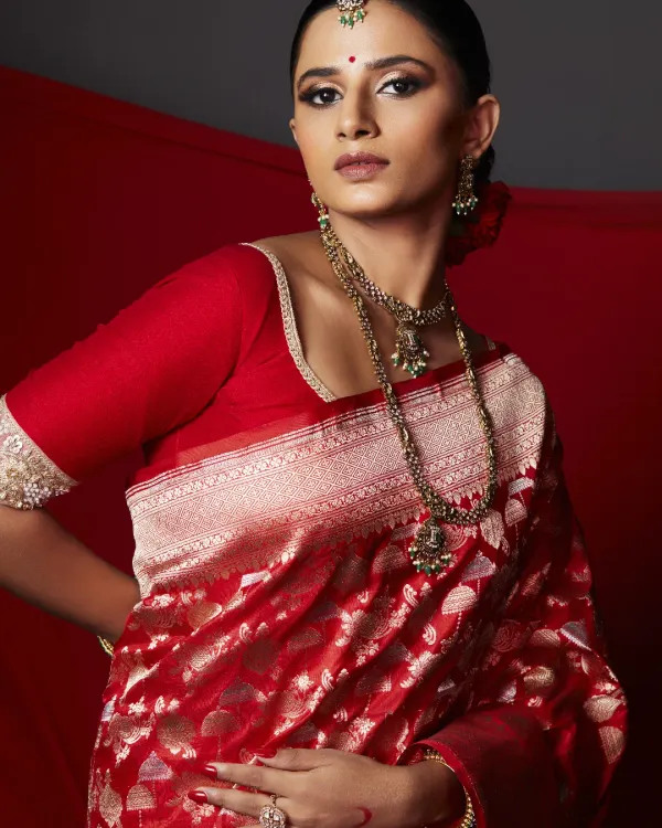 The complete royal bride ensemble. The makeup is balanced to complement the rich red and gold of the Banarasi saree, creating a look that is both majestic and deeply rooted in tradition.