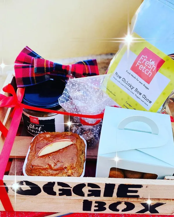 This is our Woof-Woof Doggie Box, the ultimate gift for your furry best friend. It's packed with a variety of our best treats, including cookies, a grain-free muffin, natural peanut butter, and even a stylish bow tie for special occasions.