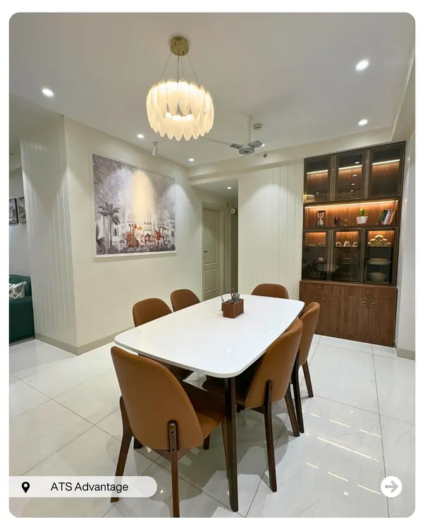 An elegant dining space featuring a white marble-top table, comfortable leatherette chairs, and a stunning feather chandelier. The glass crockery unit with internal lighting adds a touch of sophistication.