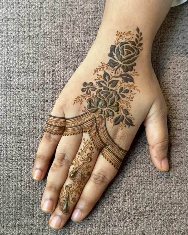 A beautiful and modern rose design. This style, often called a 'haath phool' or hand harness, connects the finger and wrist with a delicate floral trail.