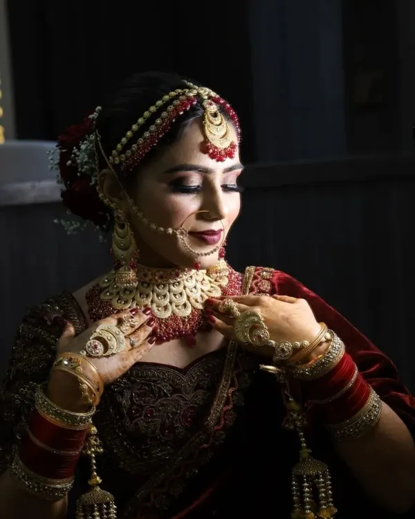 A timeless bridal look featuring flawless HD makeup with a focus on radiant skin and defined eyes. The deep red lip and traditional jewellery complete this classic Indian bride's portrait, captured in professional lighting to showcase every detail.