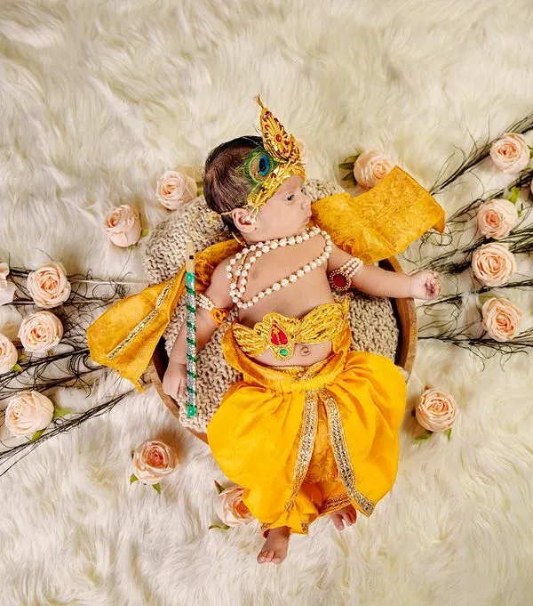 A beautifully styled overhead shot of a newborn dressed as Krishna, surrounded by peacock feathers and roses. Our themed shoots are carefully designed to create stunning, artistic portraits.