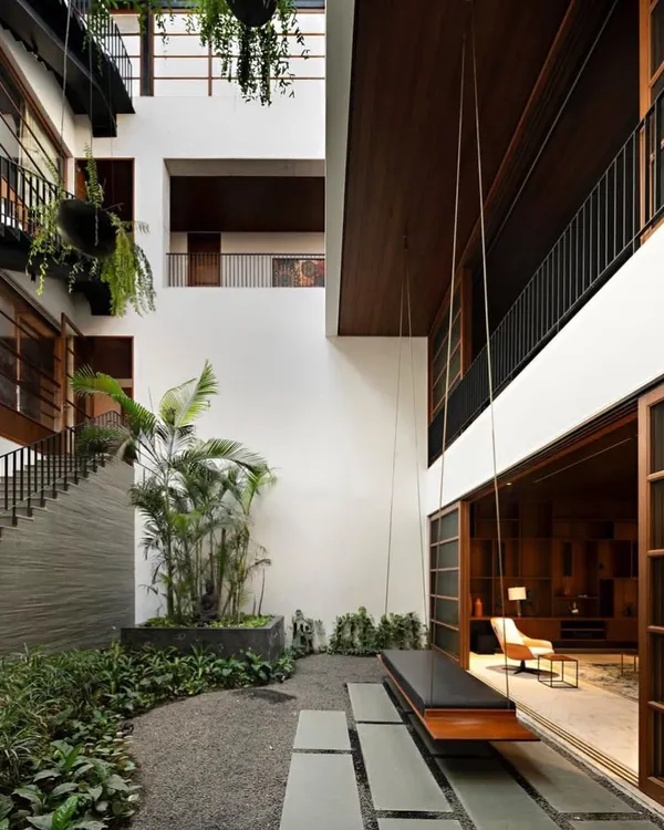 This central courtyard is designed as an open-to-sky sanctuary within the home. The use of gravel, stone pavers, and a mix of hanging and potted plants creates a multi-layered green space that connects different levels of the house.