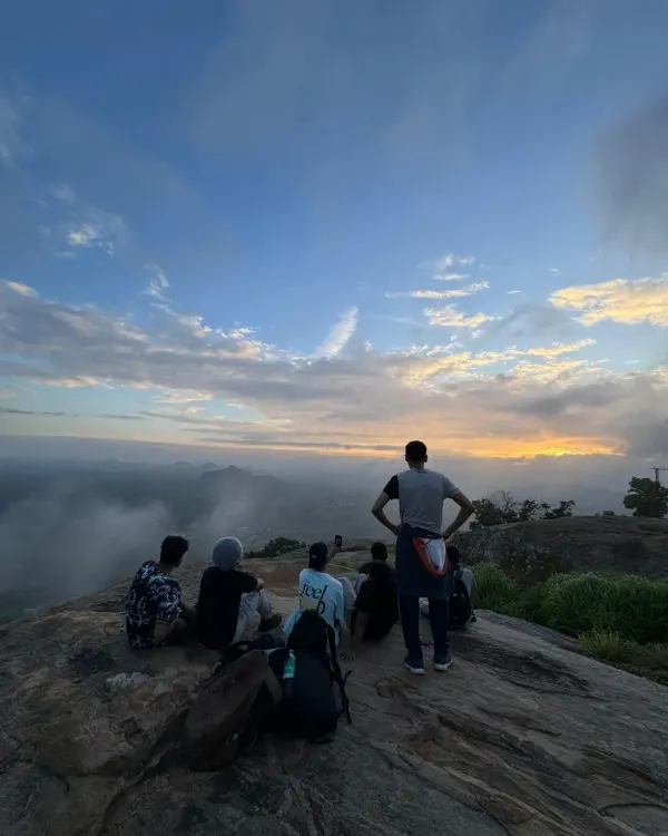 A group of trekkers sits together on a rocky summit, watching the sun rise through the clouds. This is the kind of magic we create, moments of peace and connection high above the everyday.