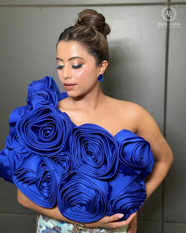 A close-up of the modern glam look, highlighting the flawless glass skin and the pop of blue from the winged eyeliner. The sleek high bun adds a touch of sophistication to the overall style.